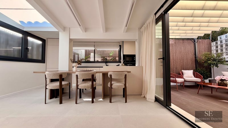 Modern dining room with wooden table and designer chairs next to a large sliding glass door opening onto a private terrace.