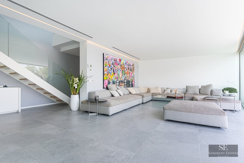 Spacious living room with large grey modular sofa, colorful wall art, and glass-railing staircase.