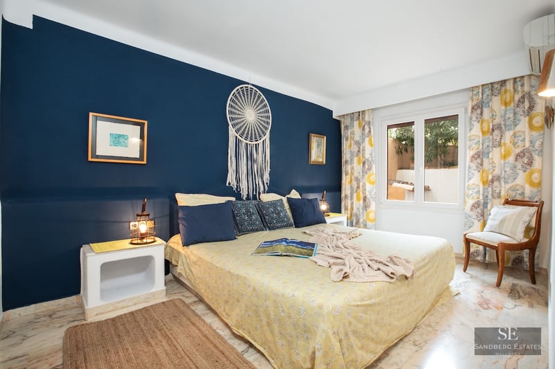 Bedroom featuring a large bed, navy blue accent wall with a dreamcatcher, and polished marble flooring.
