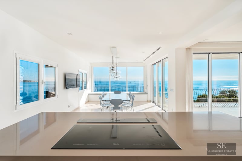 Close-up of a sleek kitchen counter with an induction hob, looking out towards a dining area and a wide blue sea view.
