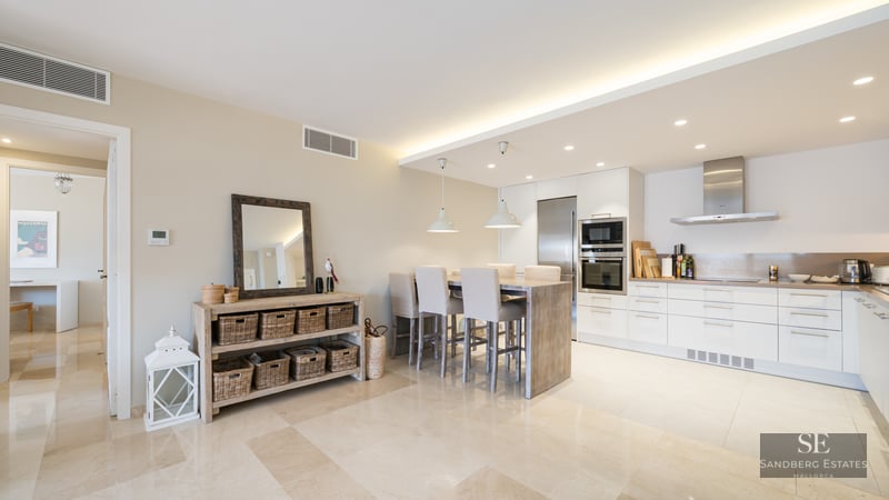 Bright modern kitchen with white cabinets, stainless steel appliances, and a wooden dining island with high chairs.