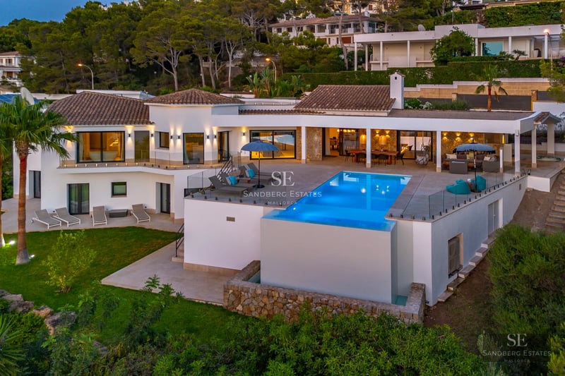 Spacious living room featuring floor-to-ceiling windows, beige sofas, a modern fireplace, and panoramic views. Abundant natural light.