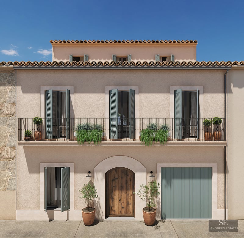 Three-story facade with beige stucco walls, sage green shutters, wrought iron balcony, and arched wooden door.