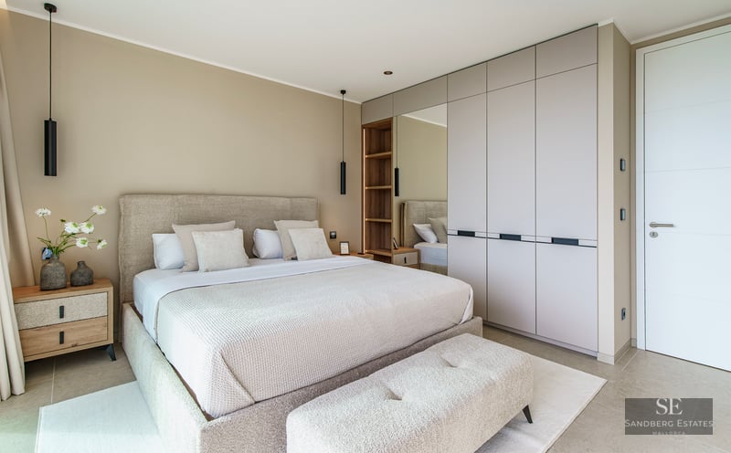 Modern bedroom featuring a large beige upholstered bed, minimalist built-in closets, and elegant black pendant lighting.