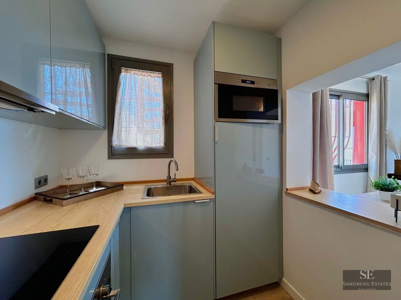 Modern kitchen with light blue cabinets, wooden countertop, stainless steel sink, and integrated microwave.