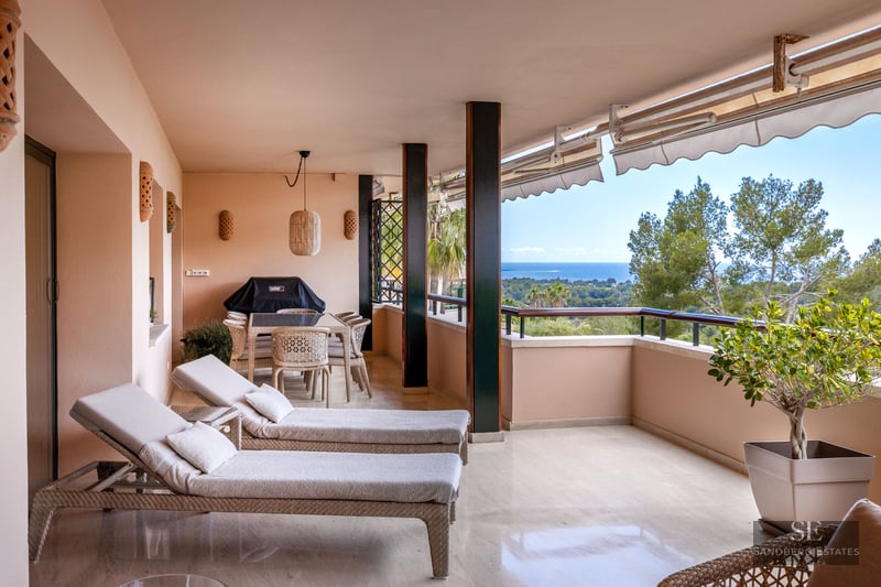 Terrasse couverte avec bains de soleil, salle à manger extérieure et vue sur la mer et la verdure.