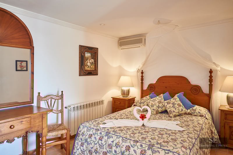 Cozy bedroom with a wooden bed, white mosquito net canopy, floral bedding, and rustic wooden furniture.
