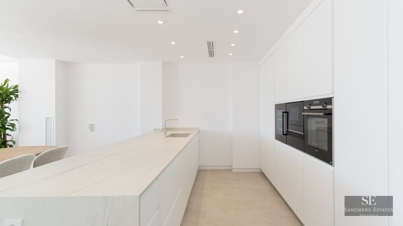 Modern minimalist white kitchen featuring a large marble island and high-end integrated appliances.