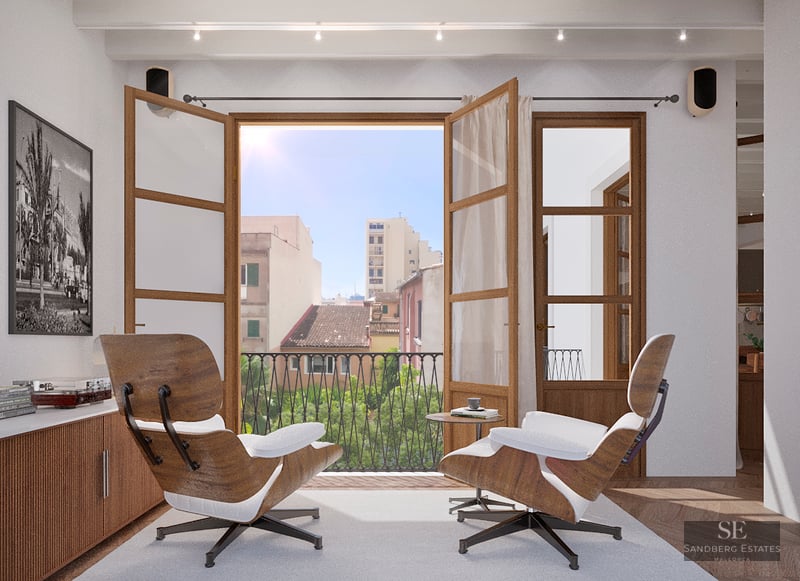 Bright living room with two Eames chairs facing an open balcony overlooking a Mediterranean city.