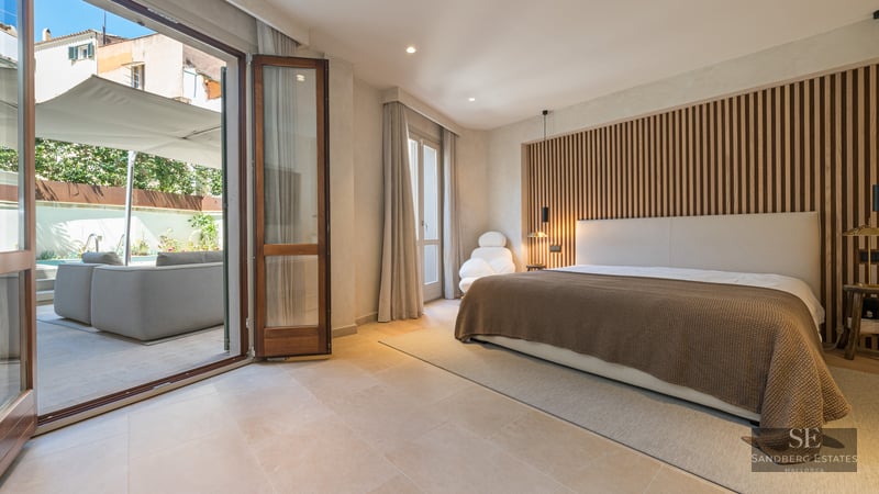 Modern master bedroom with wooden slat wall and large glass doors opening to a sunny private terrace.