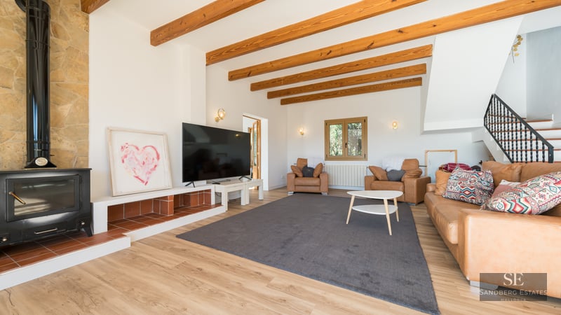 Cozy living room featuring exposed wood beams, a black wood-burning stove, tan leather sofas, and a large TV.