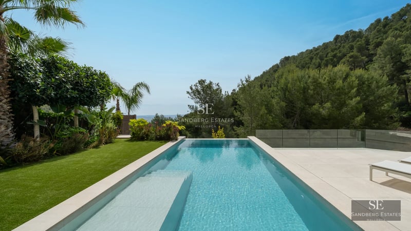 Exterior view of a modern villa featuring a reflective pool, expansive windows, and minimalist design in a landscaped setting.
