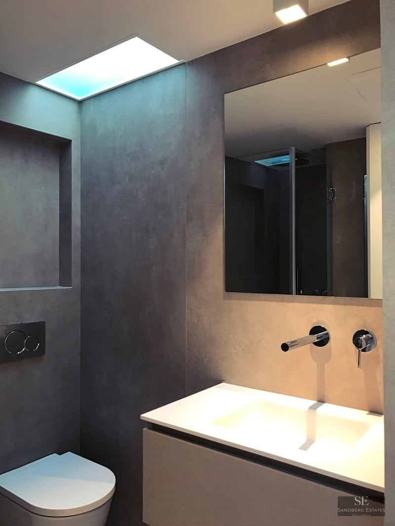 Modern bathroom featuring grey microcement walls, a white floating vanity, chrome faucet, and wall-hung toilet.