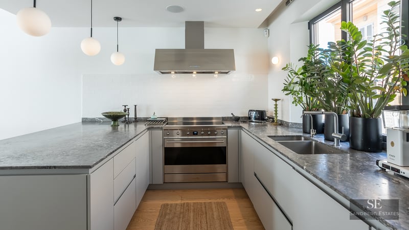 Modern U-shaped kitchen with grey stone countertops, stainless steel appliances, and natural light from a window.
