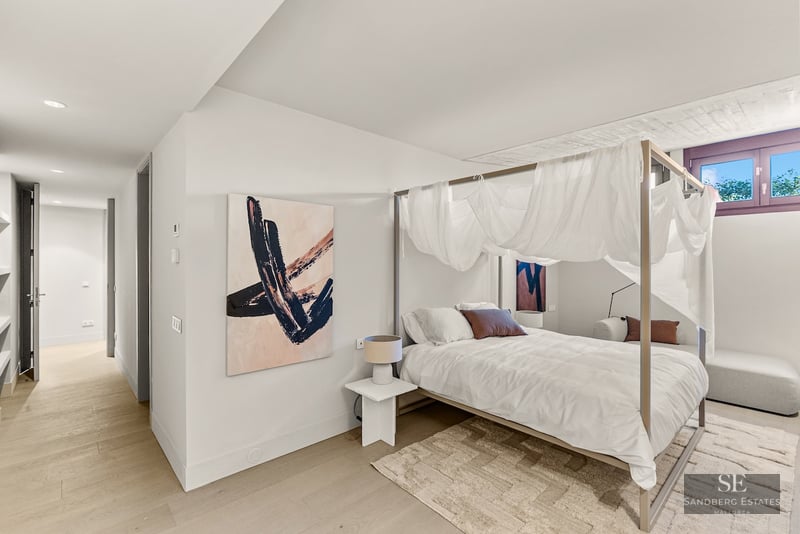 Bright bedroom featuring a four-poster canopy bed with white drapes, abstract art, and light wood flooring.