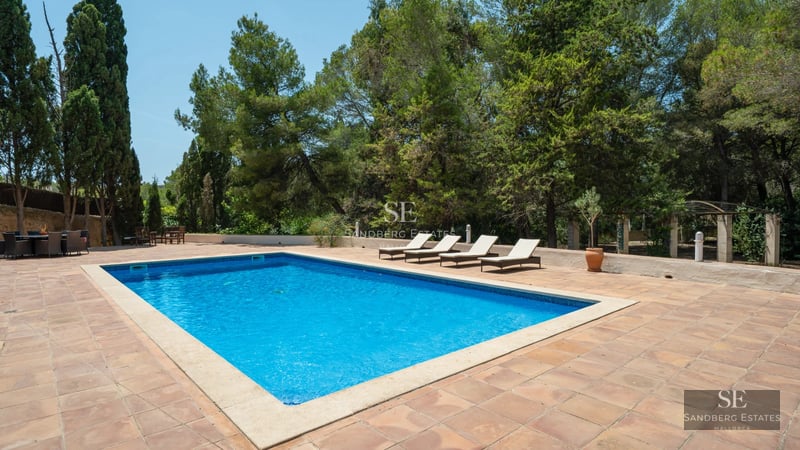 Exterior view of a modern villa with an infinity pool. Stone facade, large windows, and elegant landscaping.