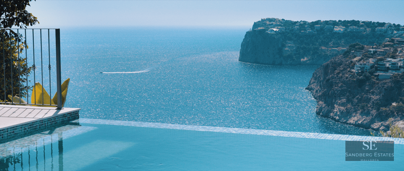 Infinity pool edge overlooking a vast blue sea with a dramatic cliffside coastline and a small boat trail.