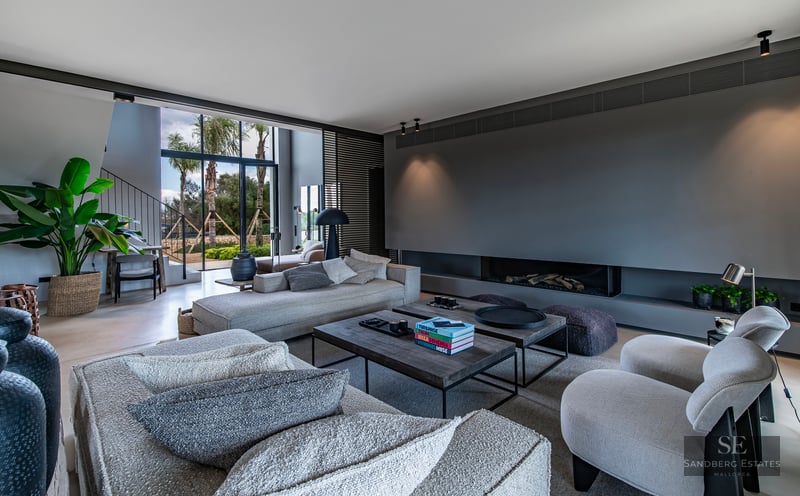 Spacious modern living room featuring gray sectional sofas, a built-in fireplace, and large windows framing palm trees.
