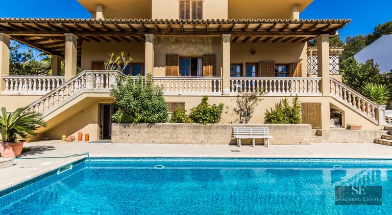 Mediterranean style villa with a large blue swimming pool and a stone balustrade terrace.