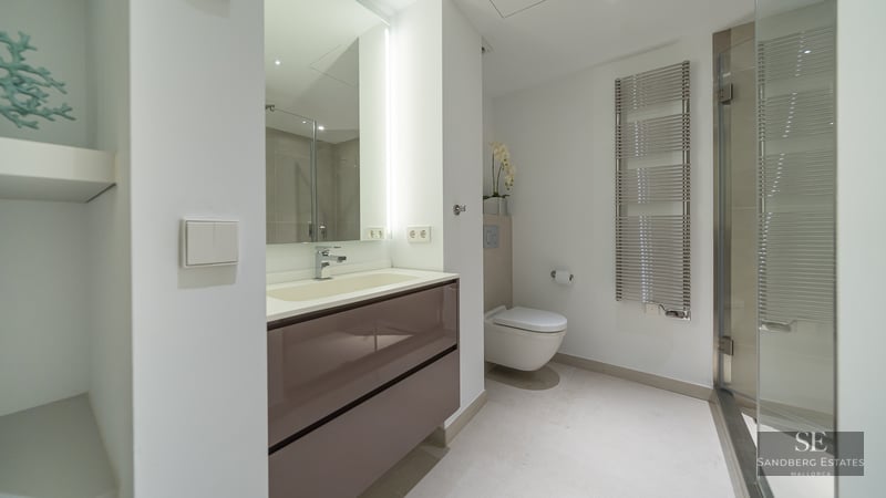 Contemporary bathroom featuring a taupe vanity, illuminated mirror, wall-hung toilet, and chrome heated towel rail.