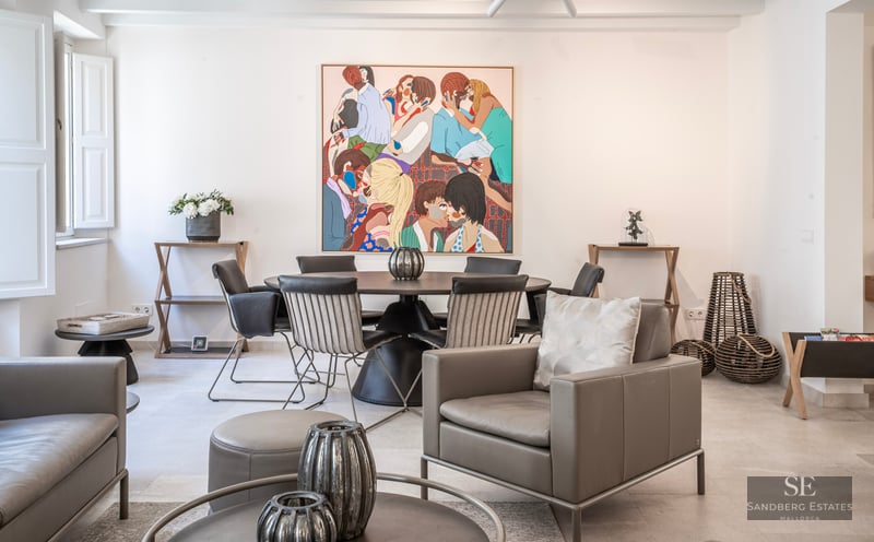 Pièce moderne lumineuse avec un fauteuil en cuir gris, une table à manger ronde et un grand tableau coloré au mur.