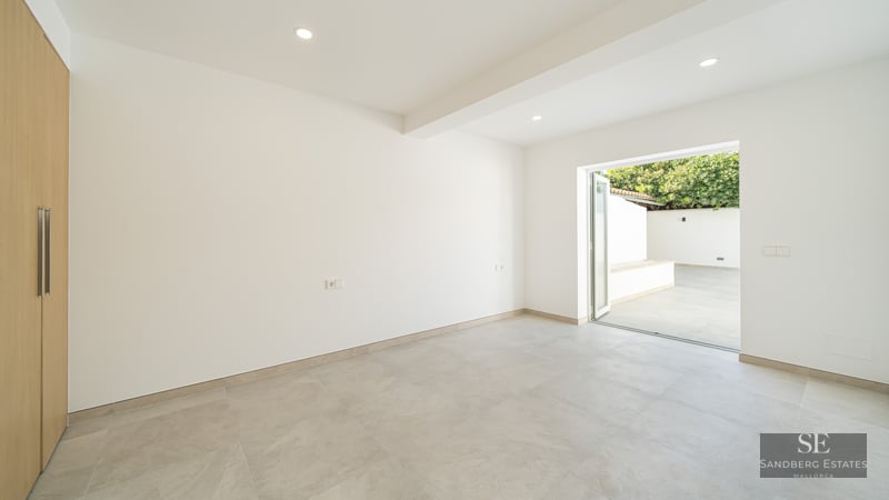 Bright, empty modern room with light gray tile floor, white walls, built-in wooden closet, and glass door to a patio.