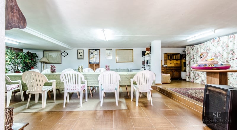 Large dining table with white chairs in a tiled room with traditional decor and floral curtains.
