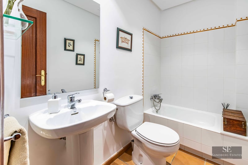 Bathroom with white wall tiles, bathtub, pedestal sink, toilet, and terracotta floor tiles.