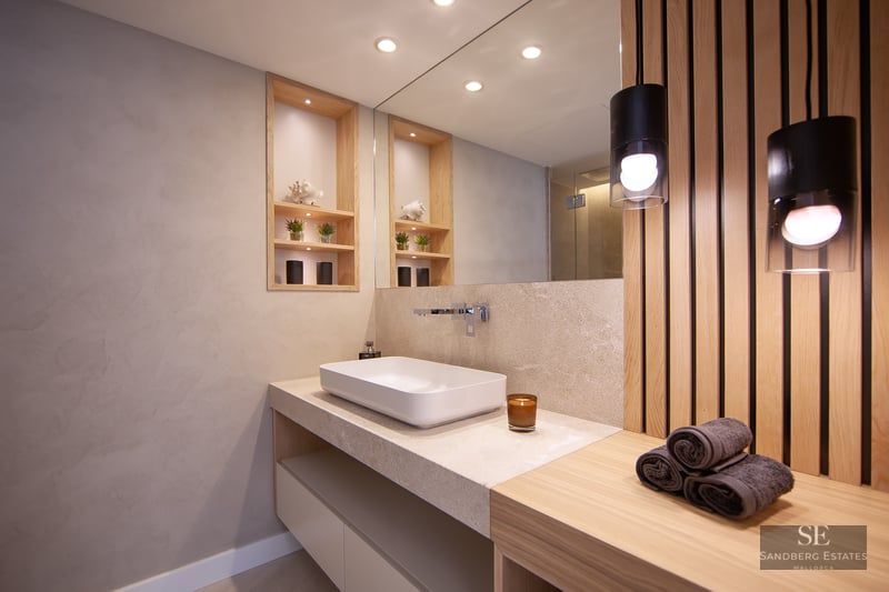 Modern bathroom featuring a white vessel sink, stone countertop, wooden slat wall, and warm pendant lighting.