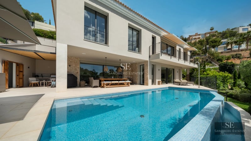 View of turquoise pool, lush garden, modern architecture, white facade, large windows, light reflections, blue sky.