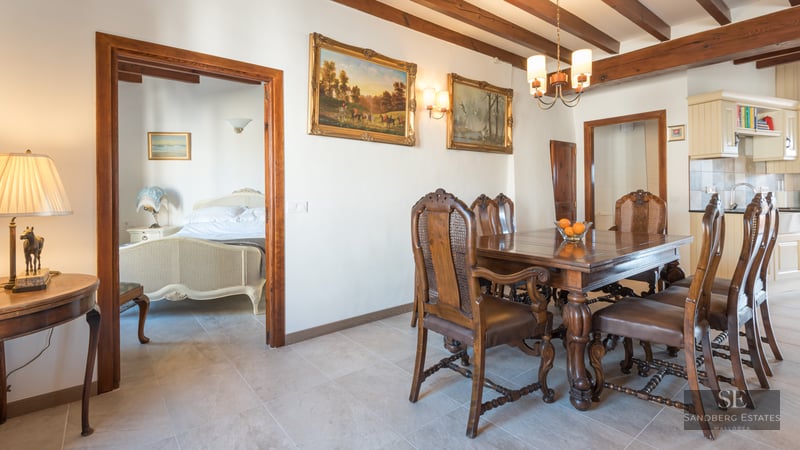 Dining room featuring a carved wood table, leather and cane chairs, beamed ceilings, and a view into a bedroom.