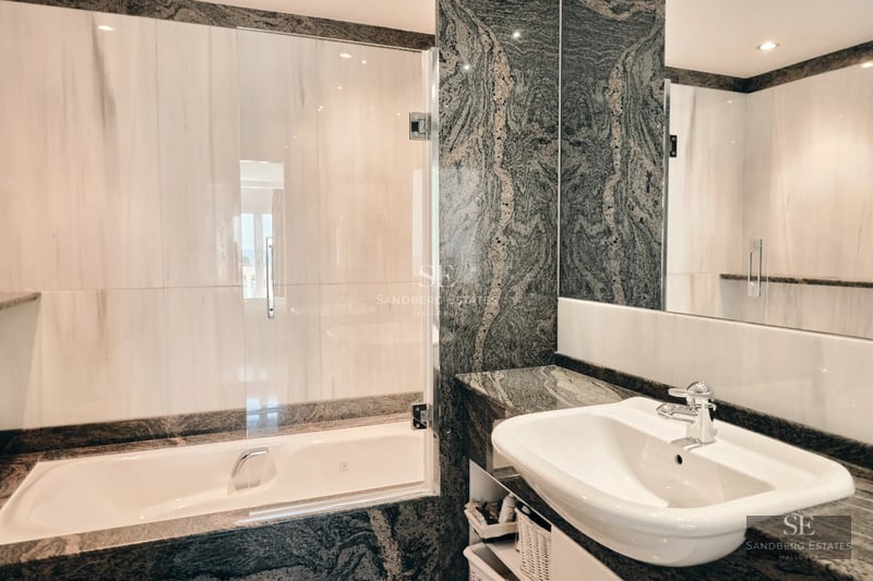 Bright, spacious living room with large windows and balcony overlooking the sea. Light wood floors and modern decor.