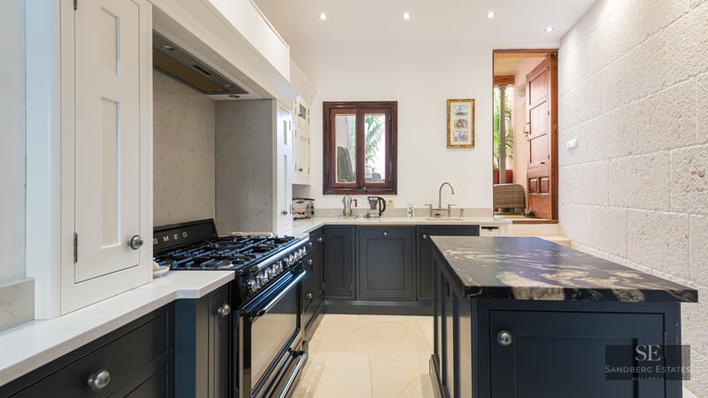 Kitchen with navy blue cabinets, white marble countertops, a Smeg range stove, and a natural stone feature wall.