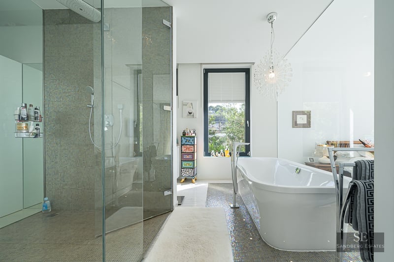Modern master bathroom featuring a glass walk-in shower and a sleek freestanding bathtub with mosaic tile flooring.