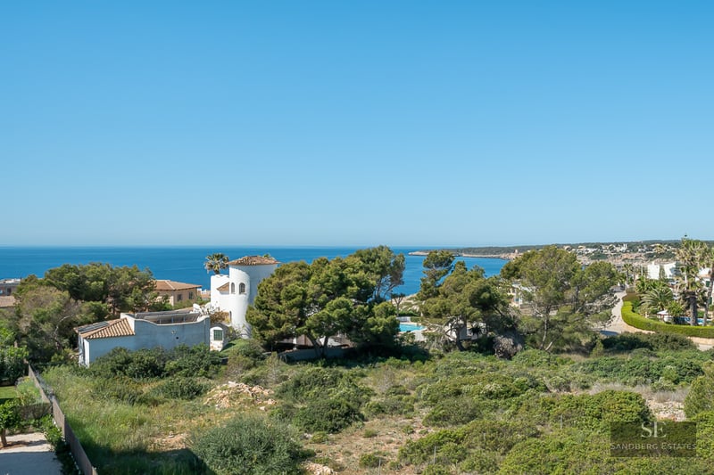 High-angle view of the blue Mediterranean sea behind lush green trees and white Mediterranean villas.