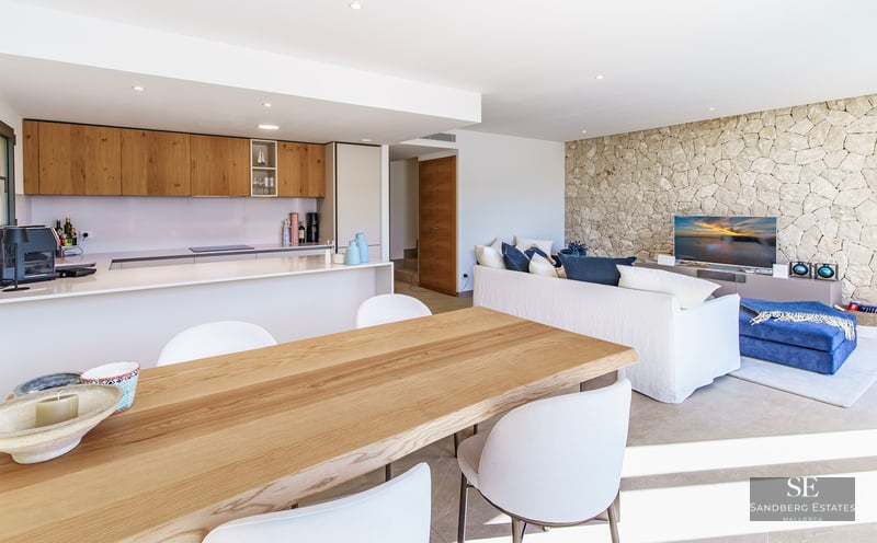 Bright open-plan room with wooden dining table, modern kitchen, white sofa, and a textured stone feature wall.