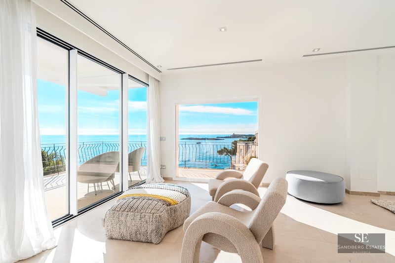 Modern white living room with designer chairs and large windows overlooking the Mediterranean sea and a terrace.