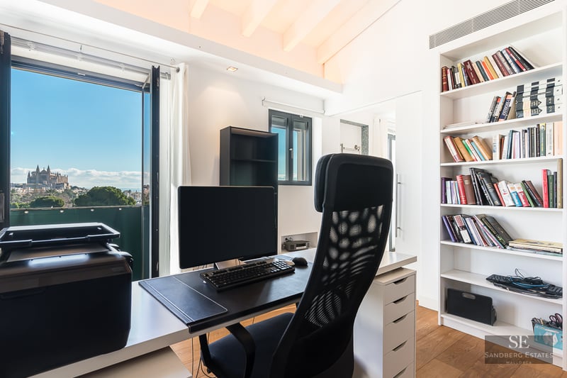 Modern home office featuring a desk, ergonomic chair, and large bookshelf overlooking the Palma Cathedral.