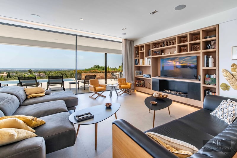 View of infinity pool surrounded by wooden deck with modern furniture. Minimalist architecture with large windows.