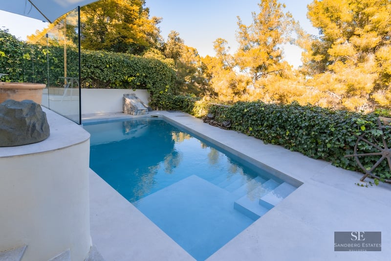 Rectangular turquoise swimming pool with integrated steps, surrounded by light stone decking and green ivy walls.