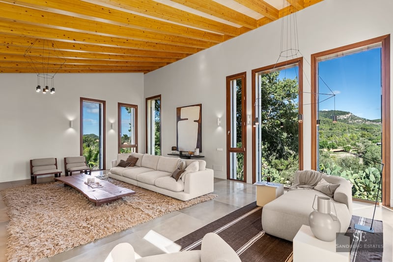 Spacious modern living room with wooden beamed ceilings, white sofas, and large windows looking out to mountains.