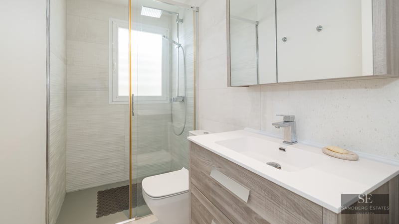 Bright bathroom featuring a wooden vanity, large mirror, and glass walk-in shower.