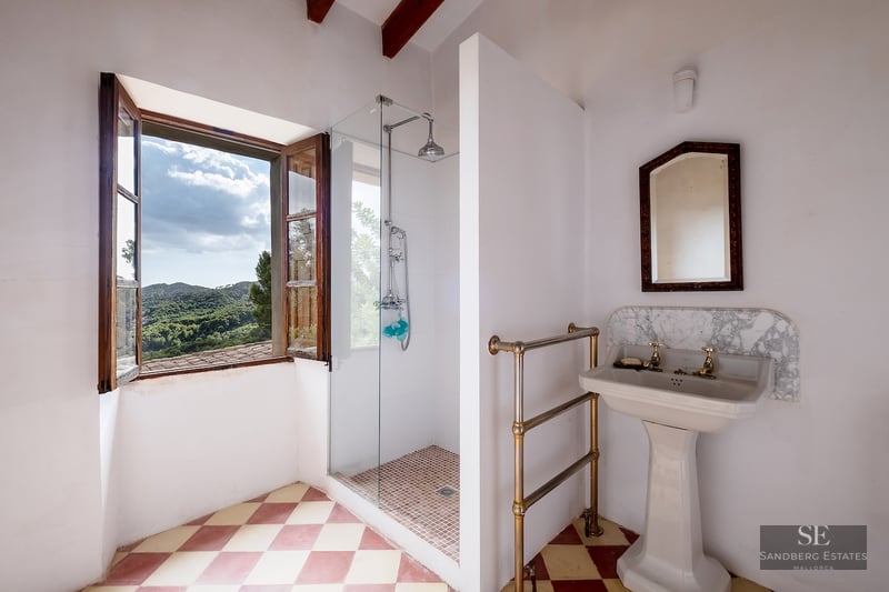 Bathroom with checkered floors, pedestal sink, and glass shower next to a window overlooking green mountains.