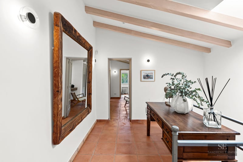 Hallway with orange tile floor, large wooden mirror, antique desk, and exposed ceiling beams.