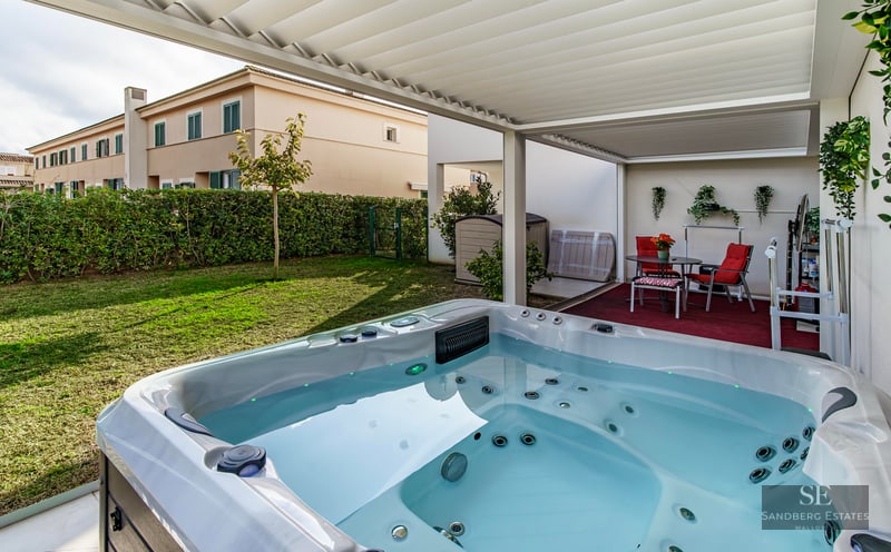 White luxury hot tub under a slatted pergola overlooking a private green garden and outdoor seating area.