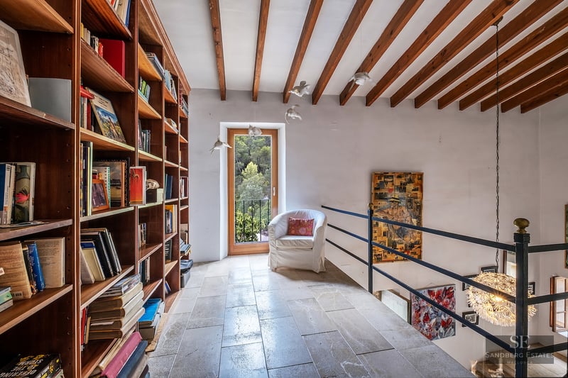 Mezzanine library featuring floor-to-ceiling wooden bookshelves, stone flooring, and rustic exposed ceiling beams.