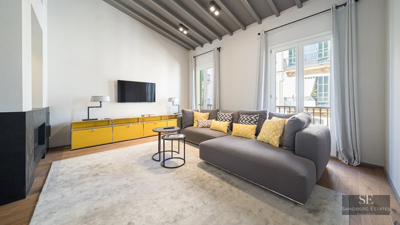 Modern living room featuring a grey sectional sofa with yellow cushions, vaulted beamed ceiling, and a fireplace.