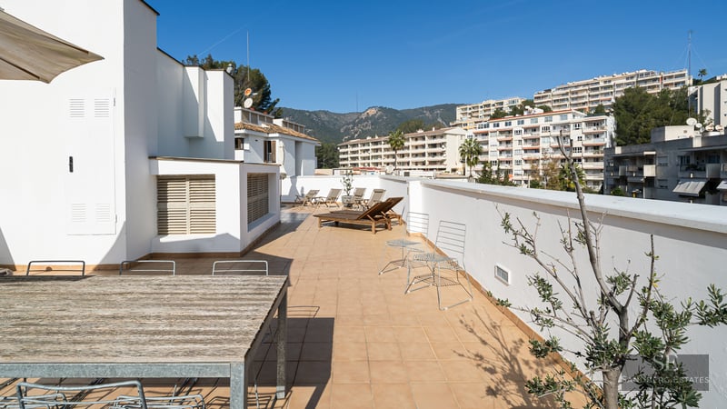 Large terrace with terracotta tiles, wooden sun loungers, and dining table under a clear blue sky.