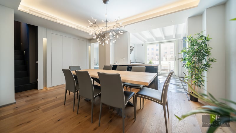 Modern dining room with a large light wood table, eight charcoal chairs, and a branch-style chandelier.
