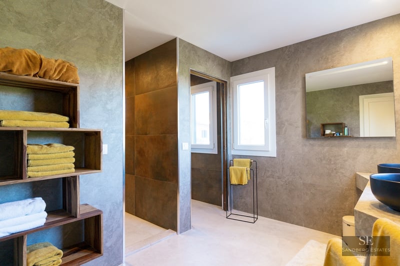 Modern bathroom featuring gray stone walls, wooden cubby shelves with yellow towels, and black vessel sinks.